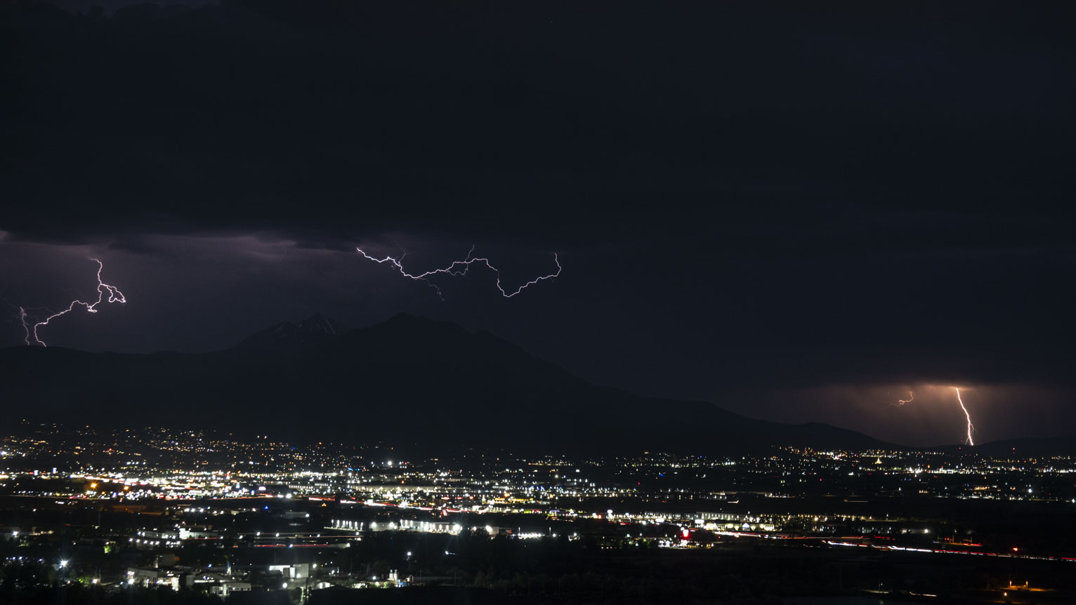 Three bolts of lightning out over the town, one is orange and two are purple